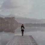 A lone figure standing beside calm water in a quiet landscape.