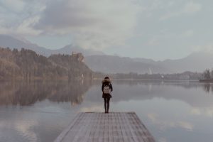 A lone figure standing beside calm water in a quiet landscape.